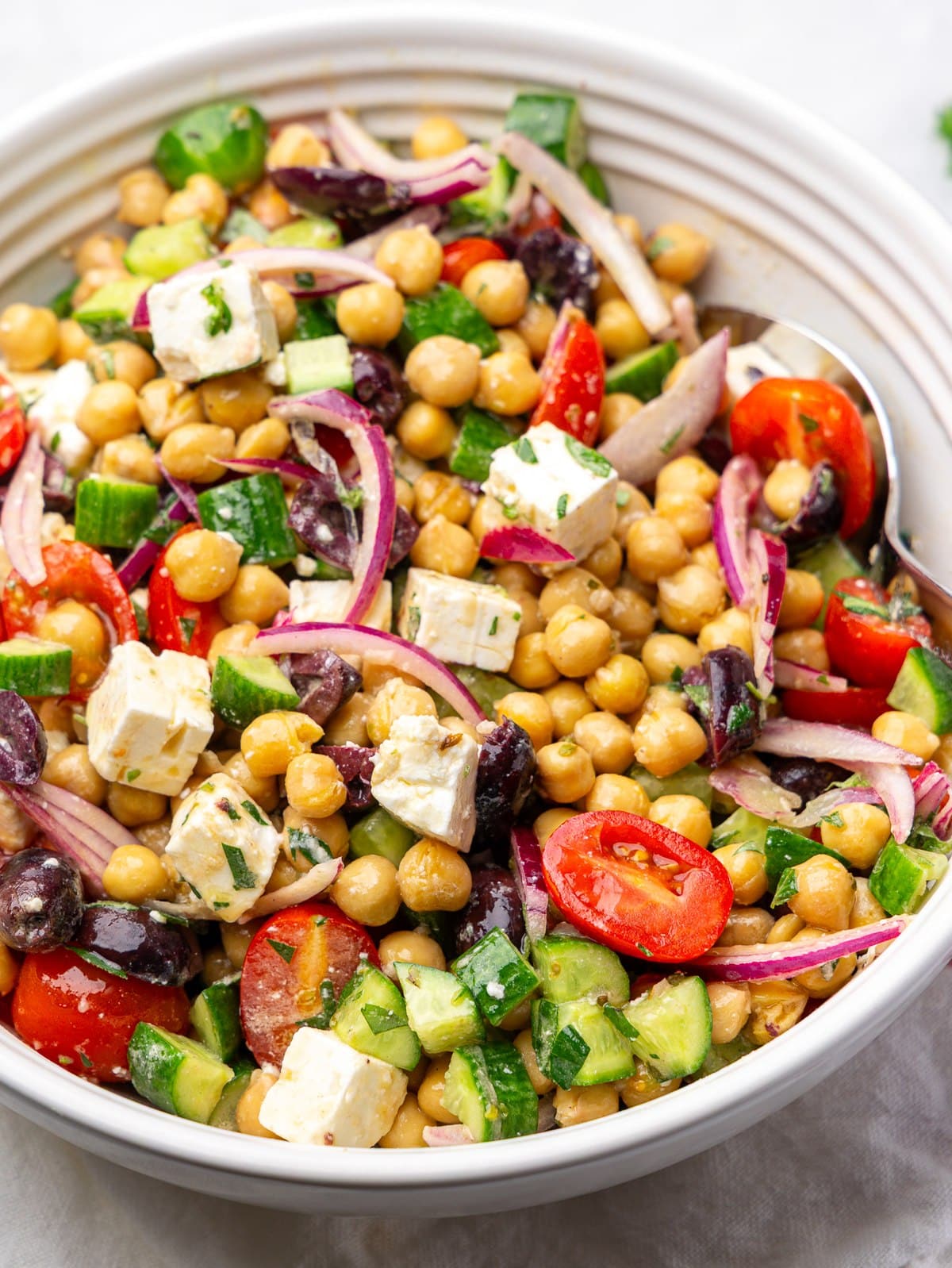 Salad with chickpeas, feta, kalamata olives, and cherry tomatoes in a white serving bowl