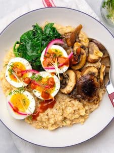 Overhead view of a savory oatmeal bowl with jammy eggs, garlicky mushrooms, wilted spinach, and microgreens