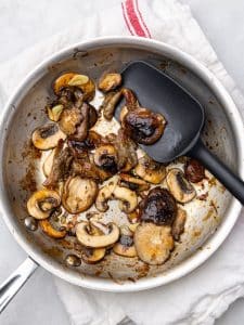 Dry-seared mixed mushrooms with sliced garlic in a stainless steel skillet