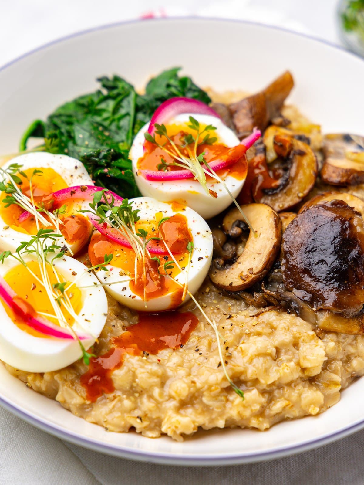 Close-up of savory oatmeal with jammy eggs, pickled red onion, microgreens, and hot sauce
