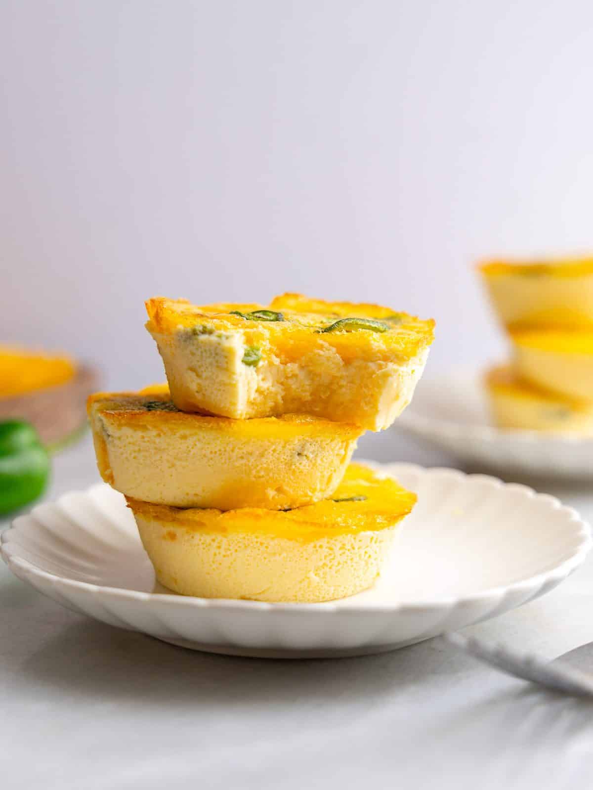 Stack of jalapeño cheddar egg bites on a white scalloped plate, the top one split open to show the soft centre