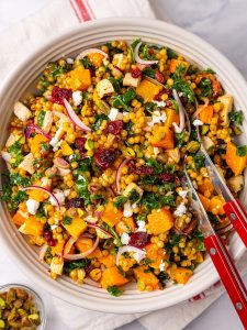 Autumn couscous salad with roasted butternut squash, kale, cranberries, feta and pearl couscous in a white bowl