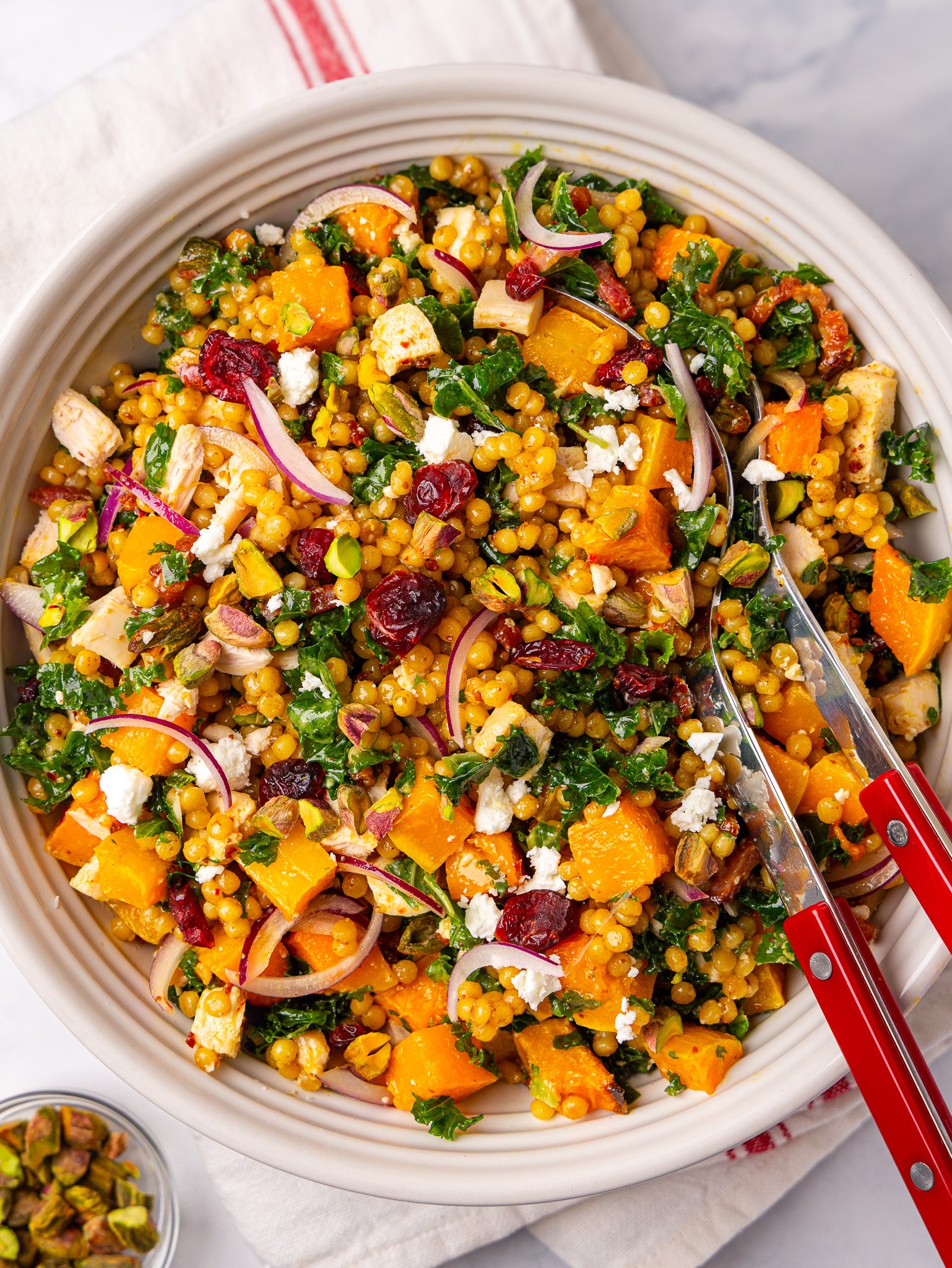 Autumn couscous salad with roasted butternut squash, kale, cranberries, feta and pearl couscous in a white bowl
