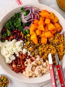 Autumn pearl couscous salad ingredients arranged in a bowl before tossing, with chicken, bacon, feta and squash