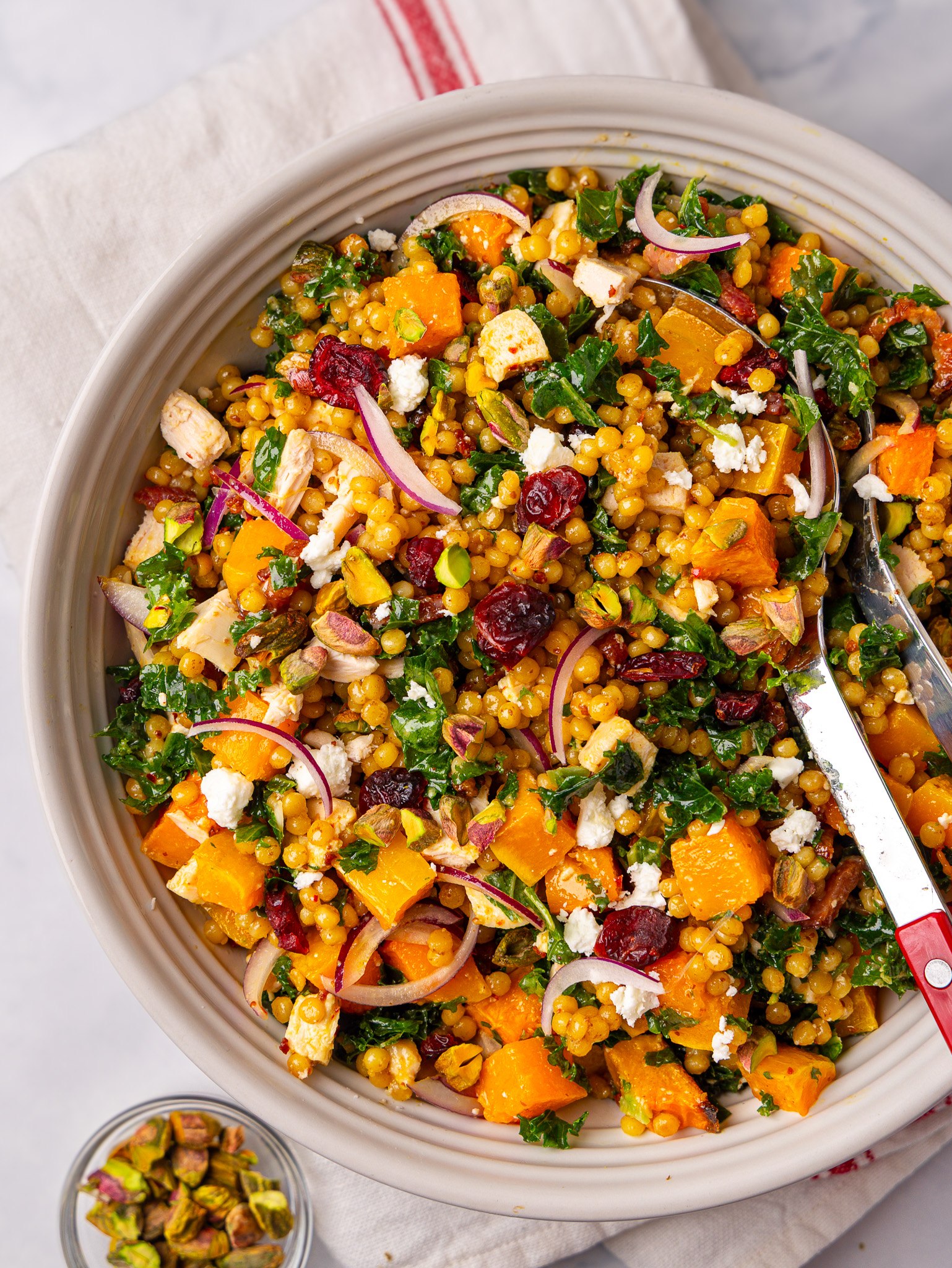 Autumn pearl couscous salad tossed with red onion, pistachios and roasted squash in a large serving bowl