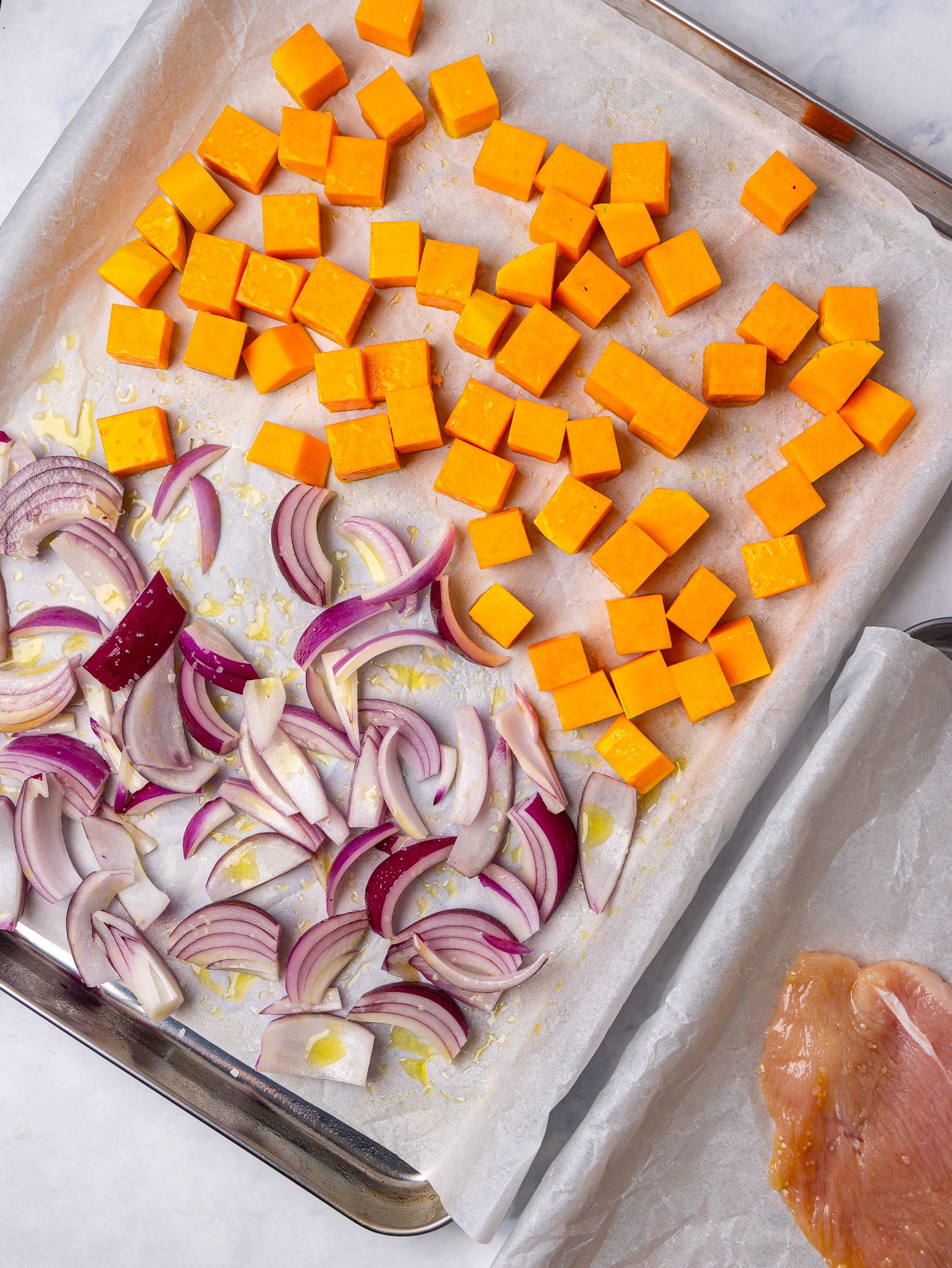 Cubed squash and sliced red onion on a sheet pan for butternut pasta salad