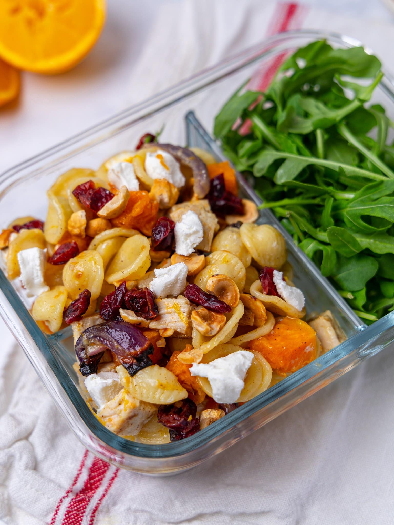 Fall harvest pasta salad in a glass meal prep container with arugula on the side