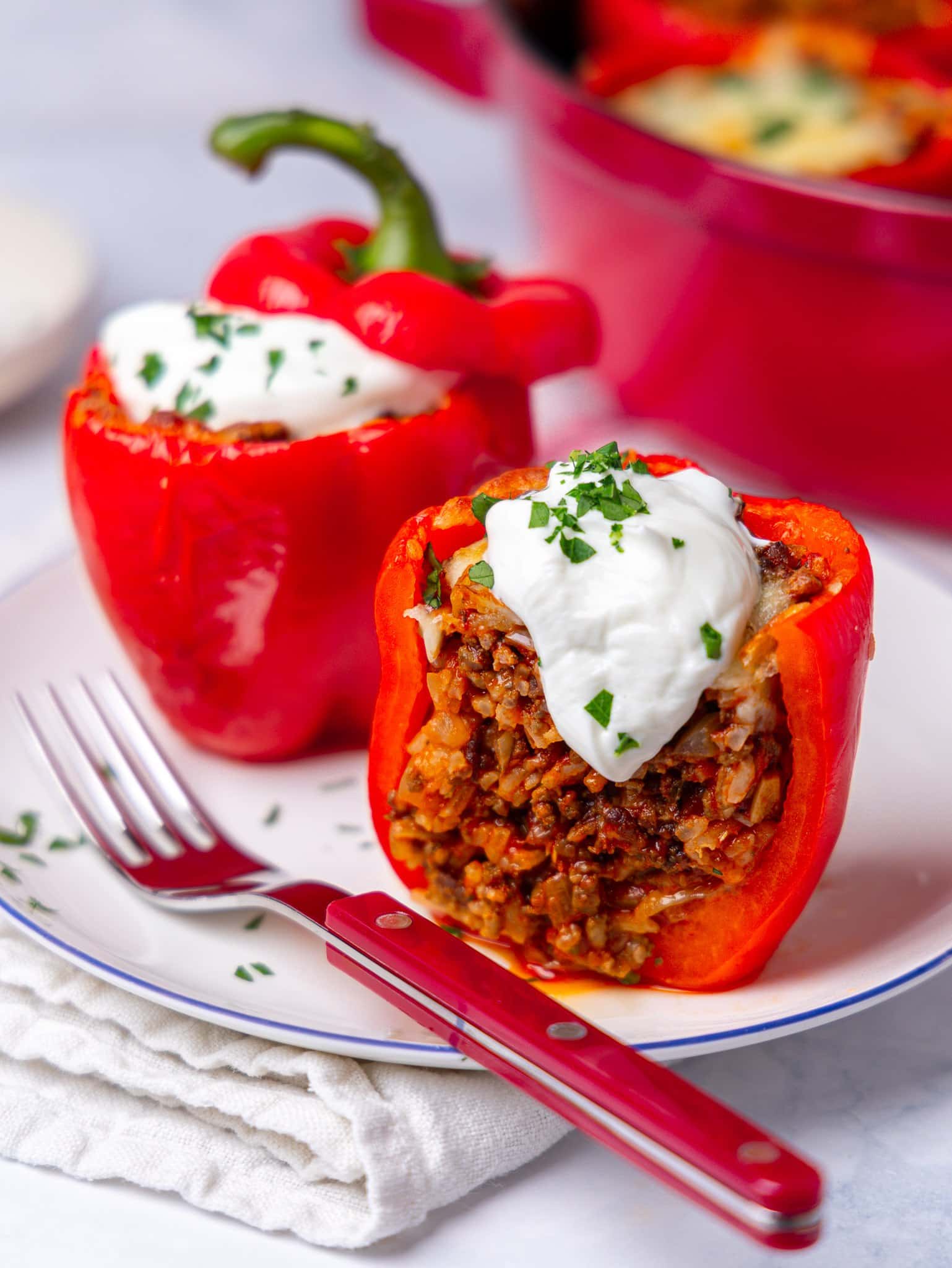 High protein stuffed peppers cut open on a plate, filled with ground beef and rice and topped with greek yogurt