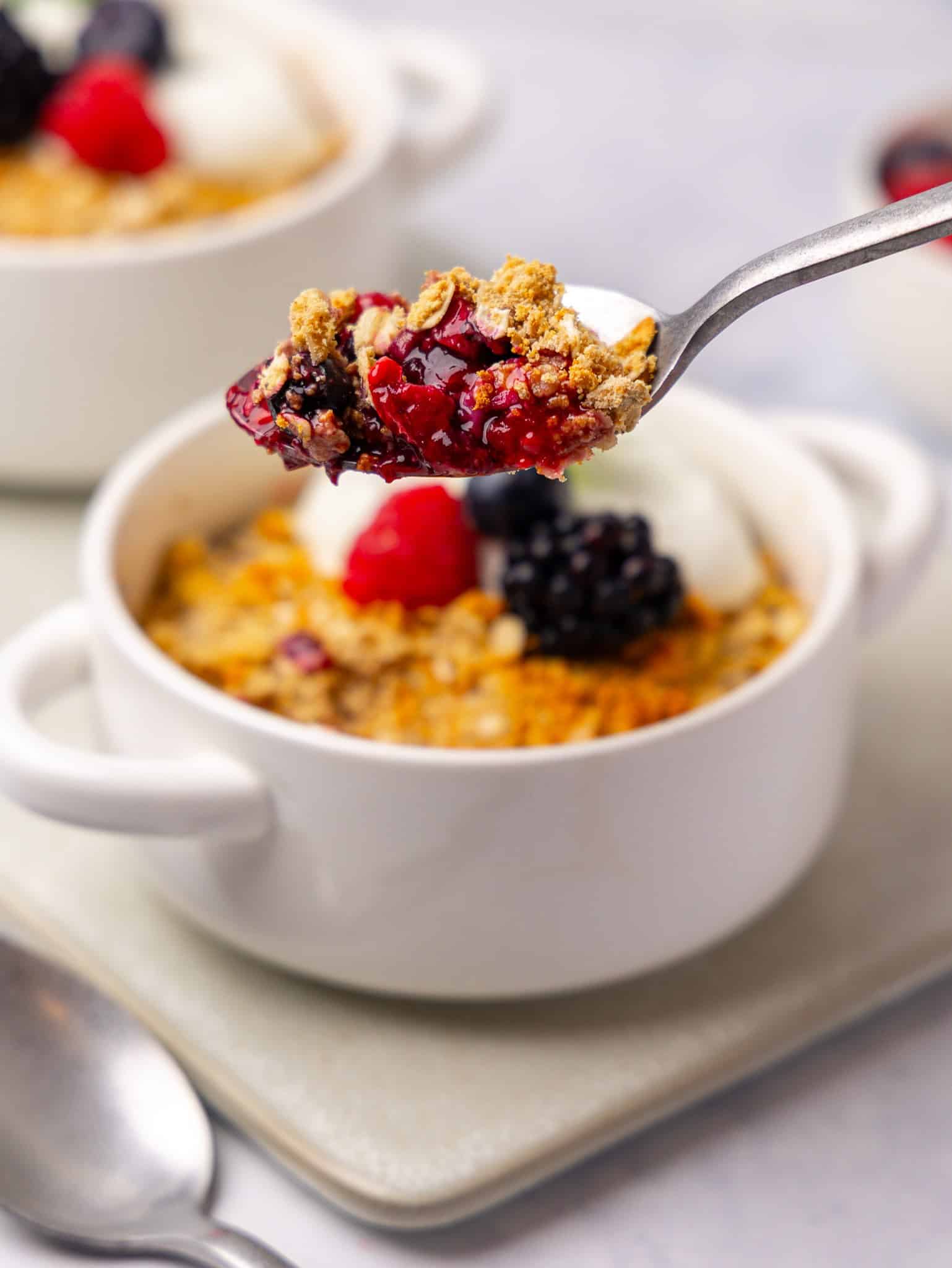 Spoonful of protein berry crumble lifted from a ramekin showing the bubbly berry filling and oat topping