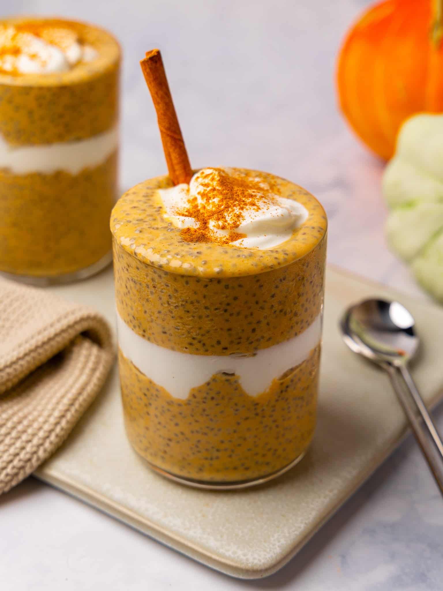 Pumpkin chia pudding with yogurt and cinnamon on top, served in a glass with a spoon