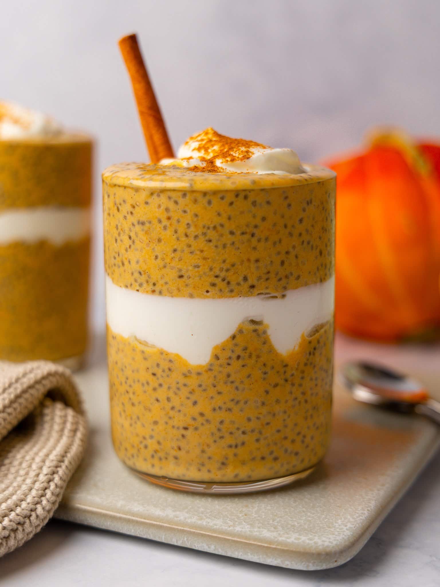 Close up of pumpkin chia pudding in a glass with a layer of yogurt and a dusting of cinnamon