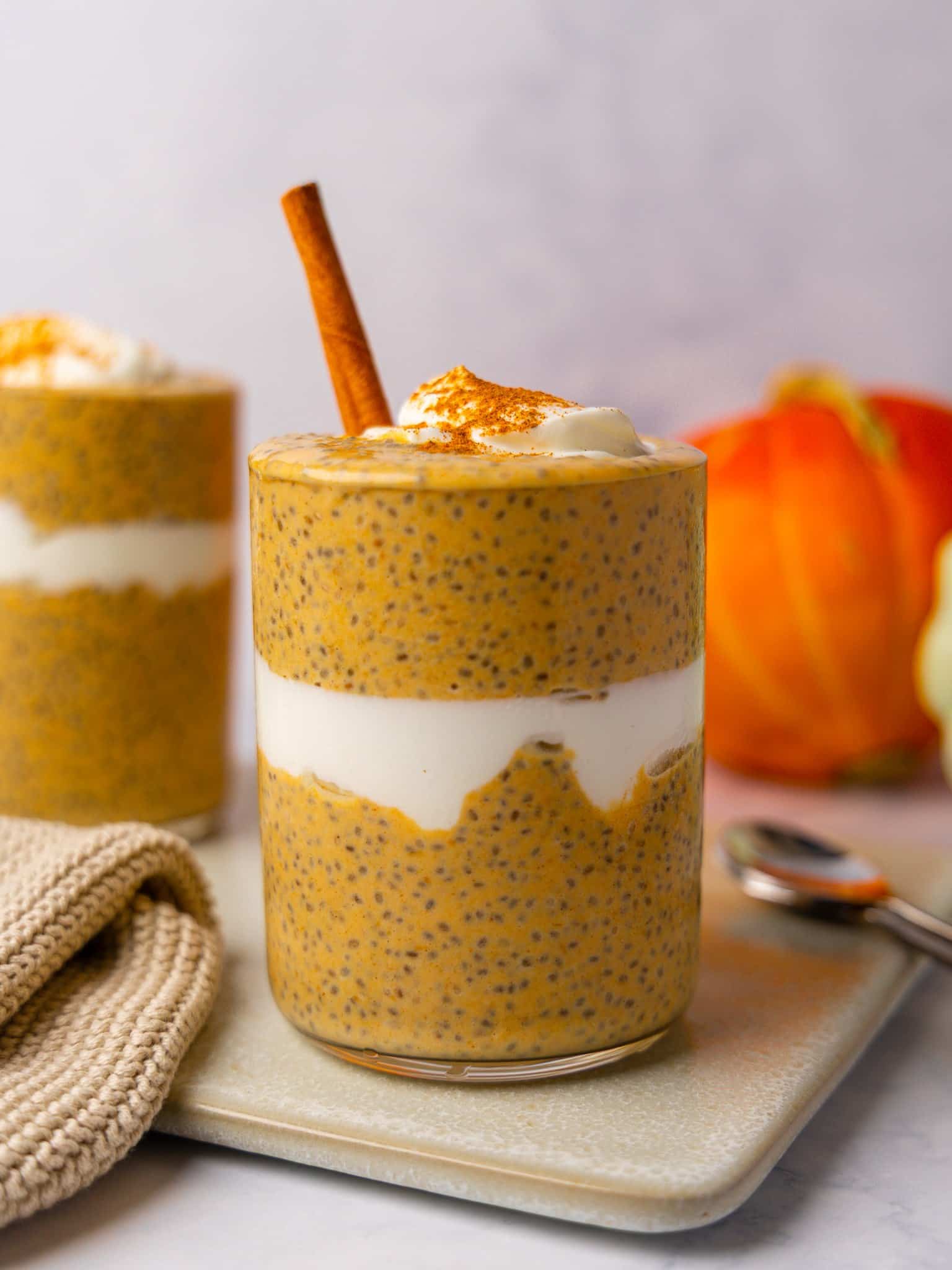 Pumpkin chia seed pudding layered with greek yogurt in a glass, topped with a cinnamon stick