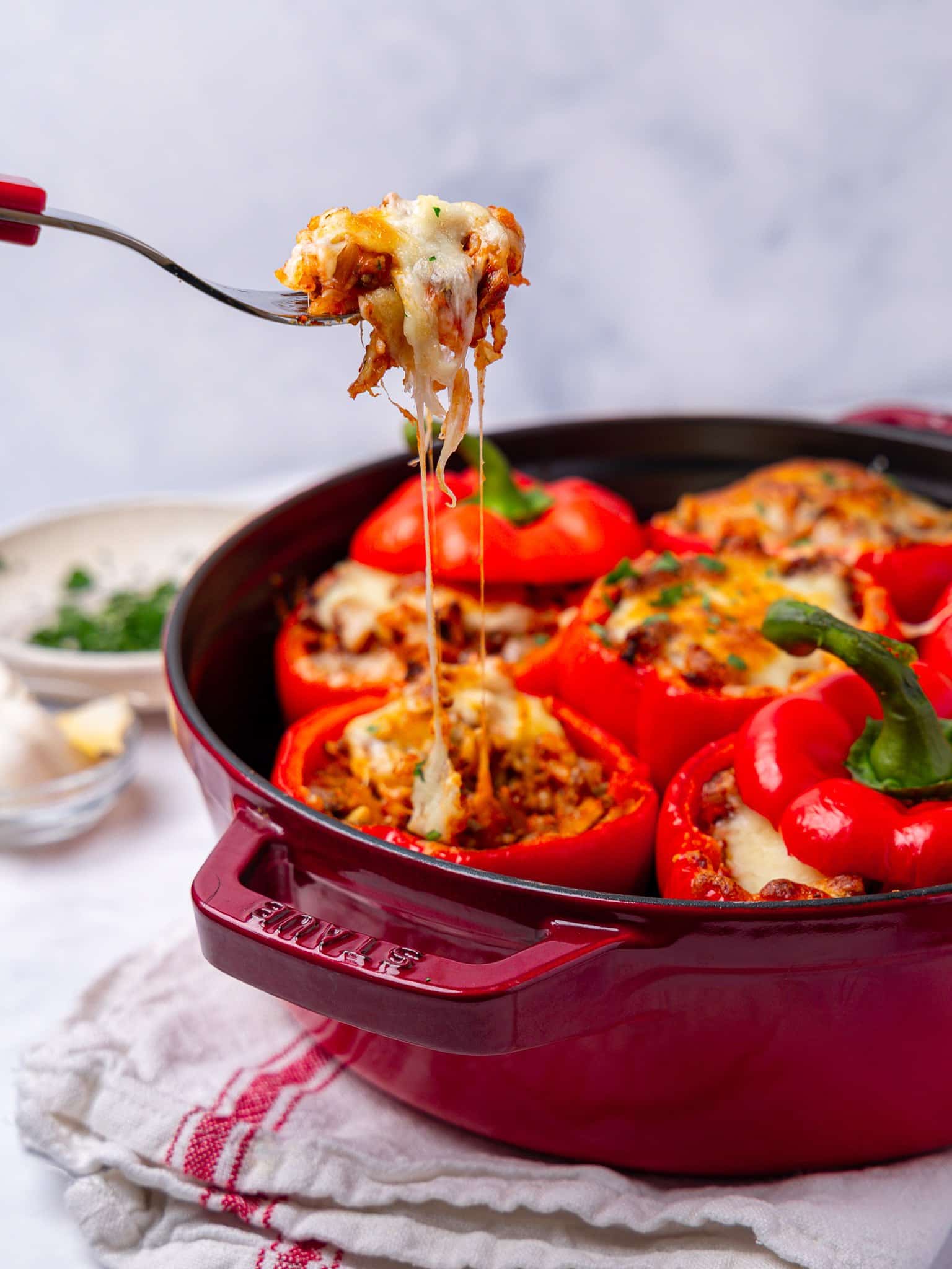 Fork lifting a bite of stuffed pepper with a long mozzarella cheese pull over the pan
