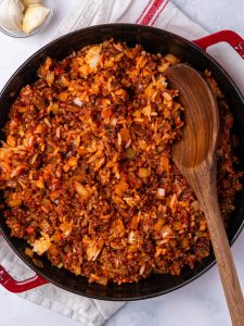 Ground beef, rice and tomato filling for a stuffed peppers recipe with rice, stirred with a wooden spoon