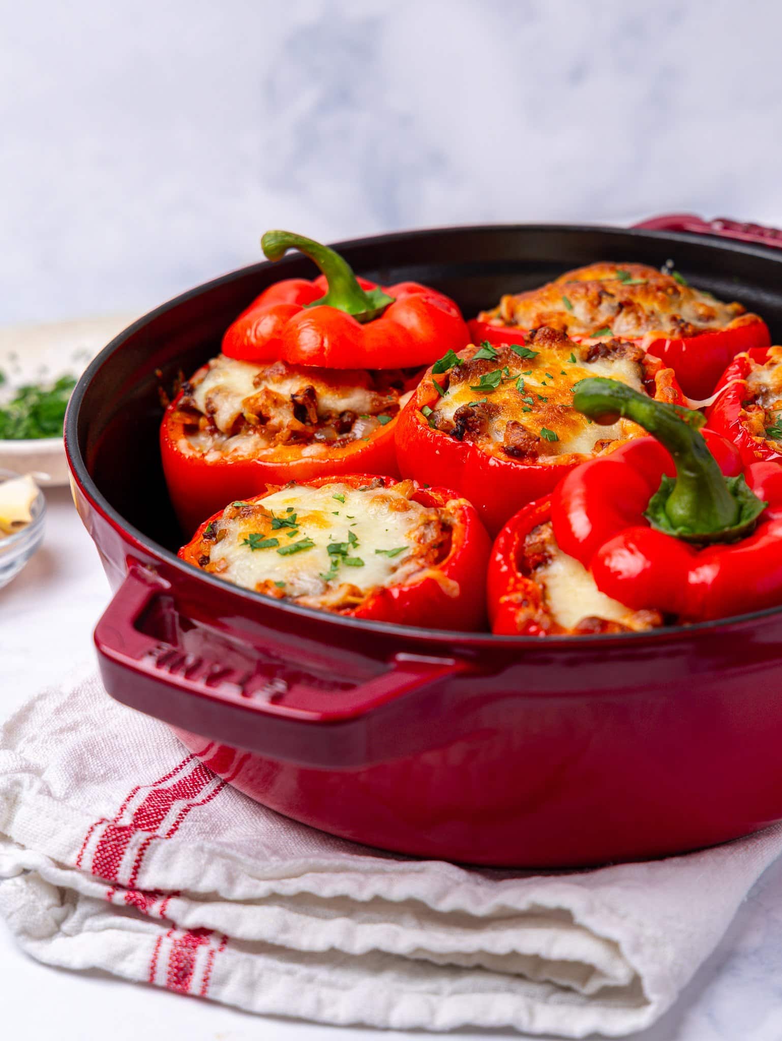 Stuffed peppers in a red cast iron pan on a striped kitchen towel