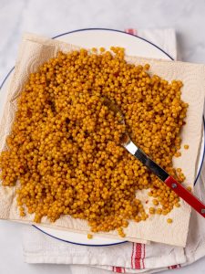 Toasted pearl couscous cooked in bone broth cooling on a paper towel-lined plate