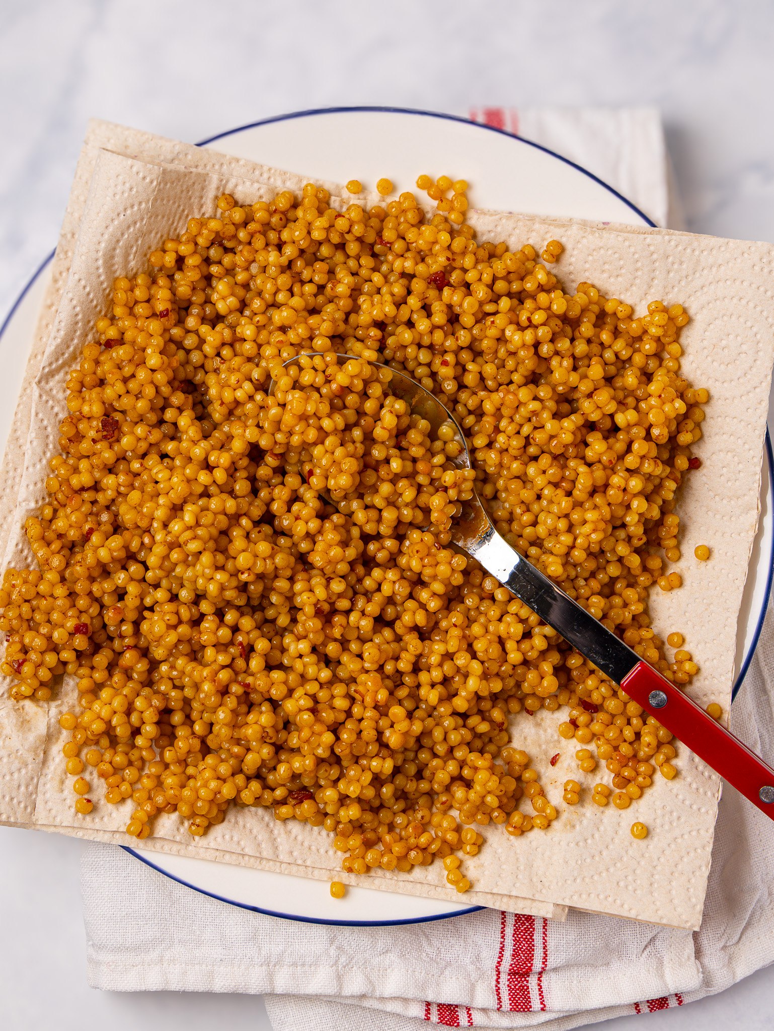 Toasted pearl couscous cooked in bone broth cooling on a paper towel-lined plate